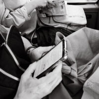 Dos personas leyendo en distintos formatos: una frente al teléfono móvil, otra en papel
